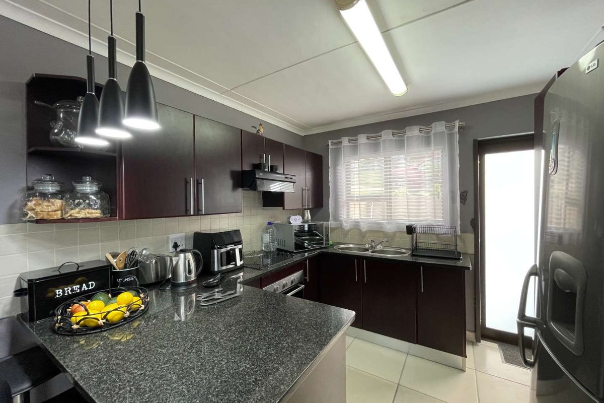 A functional kitchen featuring dark cabinetry, granite countertops, a double sink, and a built-in oven with an extractor fan.