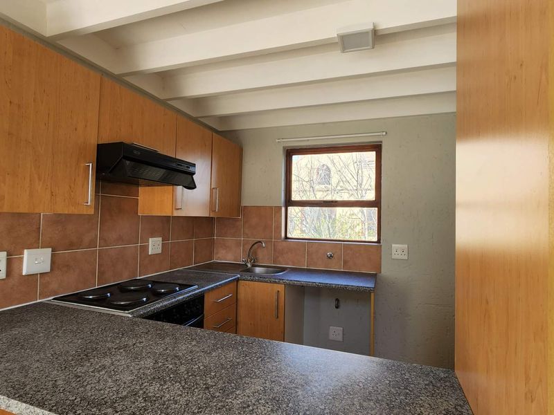 A functional kitchen featuring wood-look cabinetry, granite-style countertops, an electric hob with extractor fan, and a tiled splashback under an exposed beam ceiling.