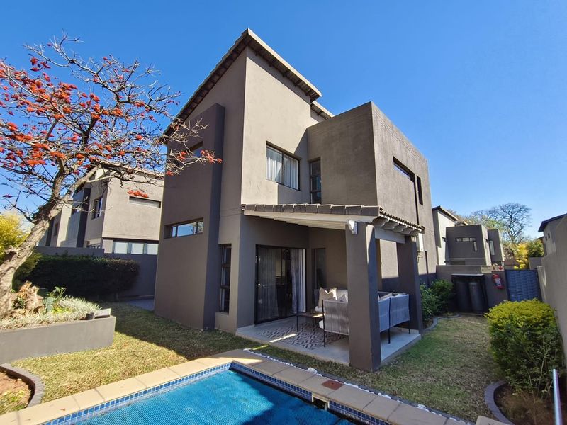 Rear view of a modern double-story house featuring a covered patio, private swimming pool, and landscaped garden area.