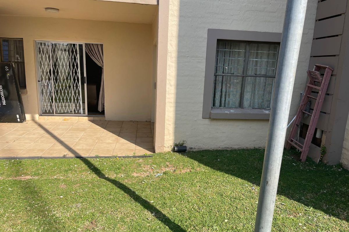 Ground floor apartment exterior featuring a tiled patio, sliding glass door with security gate, and a small private garden area.