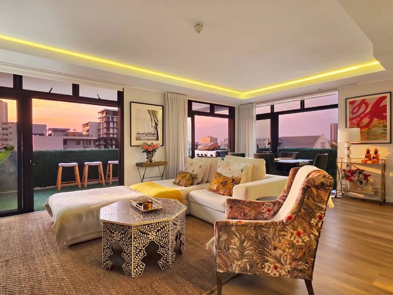 Spacious open-plan living area featuring recessed ceiling lighting, hardwood floors, and large sliding glass doors leading to a private balcony with sunset views.