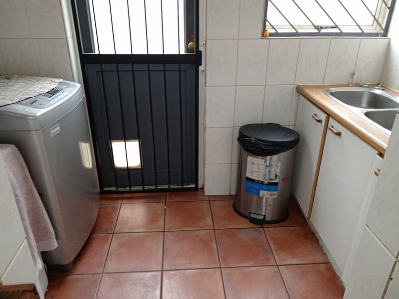 Functional laundry area featuring tiled flooring, built-in cabinetry with a stainless steel sink, and direct access to the exterior via a security gate.