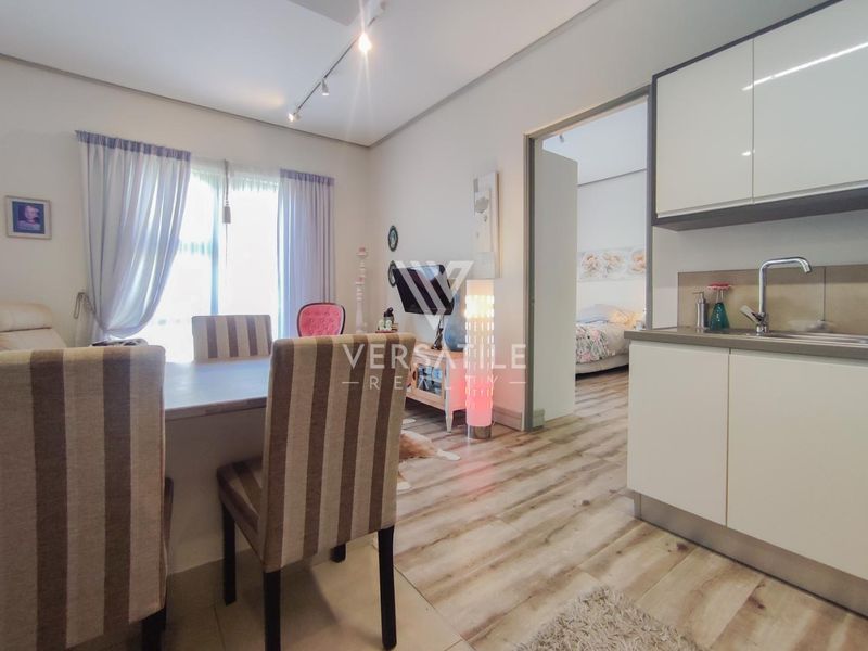 Open-plan living area featuring laminate flooring, track lighting, and a compact kitchenette with modern cabinetry and a stainless steel sink.