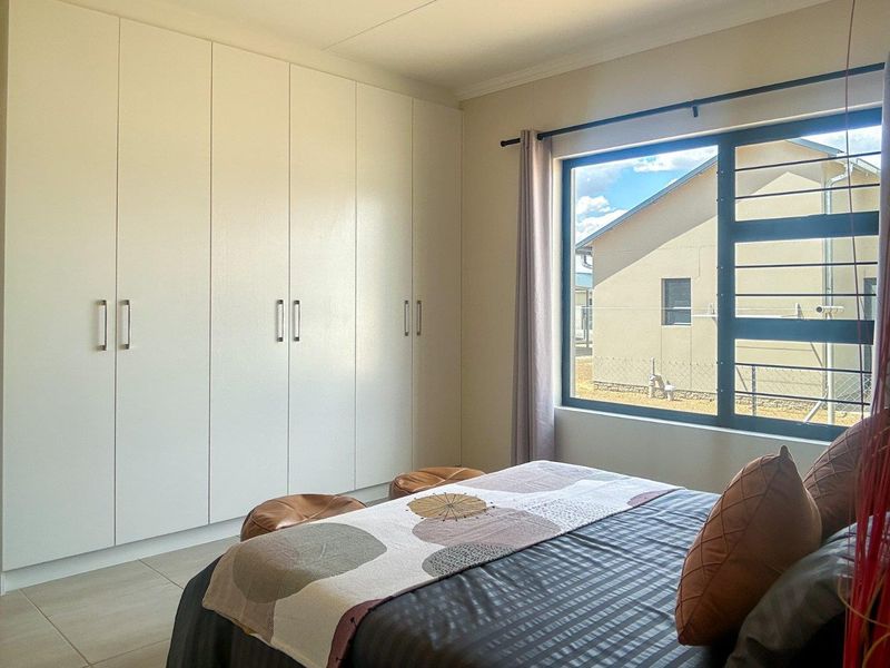 A well-maintained bedroom featuring neutral tiled flooring, ample built-in cupboard storage, and a large window providing natural light.