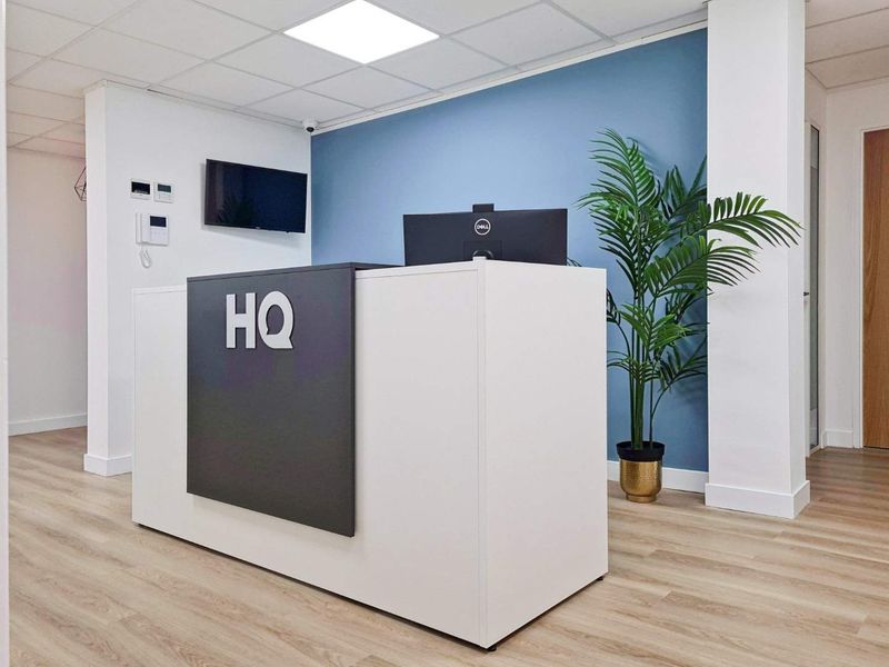Modern office reception area featuring a clean reception desk, wood-look laminate flooring, and a professional blue accent wall.