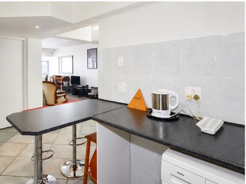 Open plan kitchen area featuring a breakfast bar, dark laminate countertops, and tiled splashbacks, flowing into the adjacent living space.
