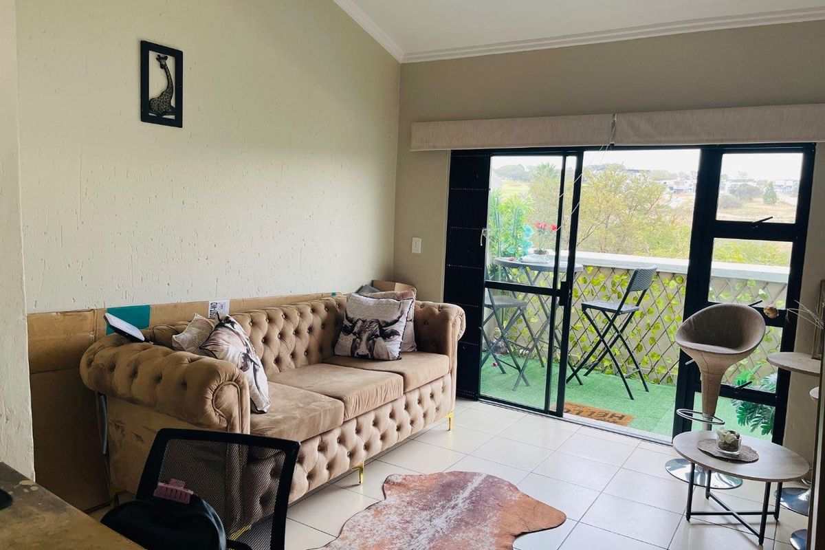 A living room featuring tiled floors, a vaulted ceiling, and a large sliding glass door providing access to a balcony.
