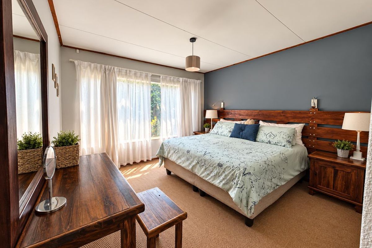 A well-maintained bedroom featuring a large window, carpeted flooring, and a custom built-in wooden headboard, creating a warm and inviting atmosphere.