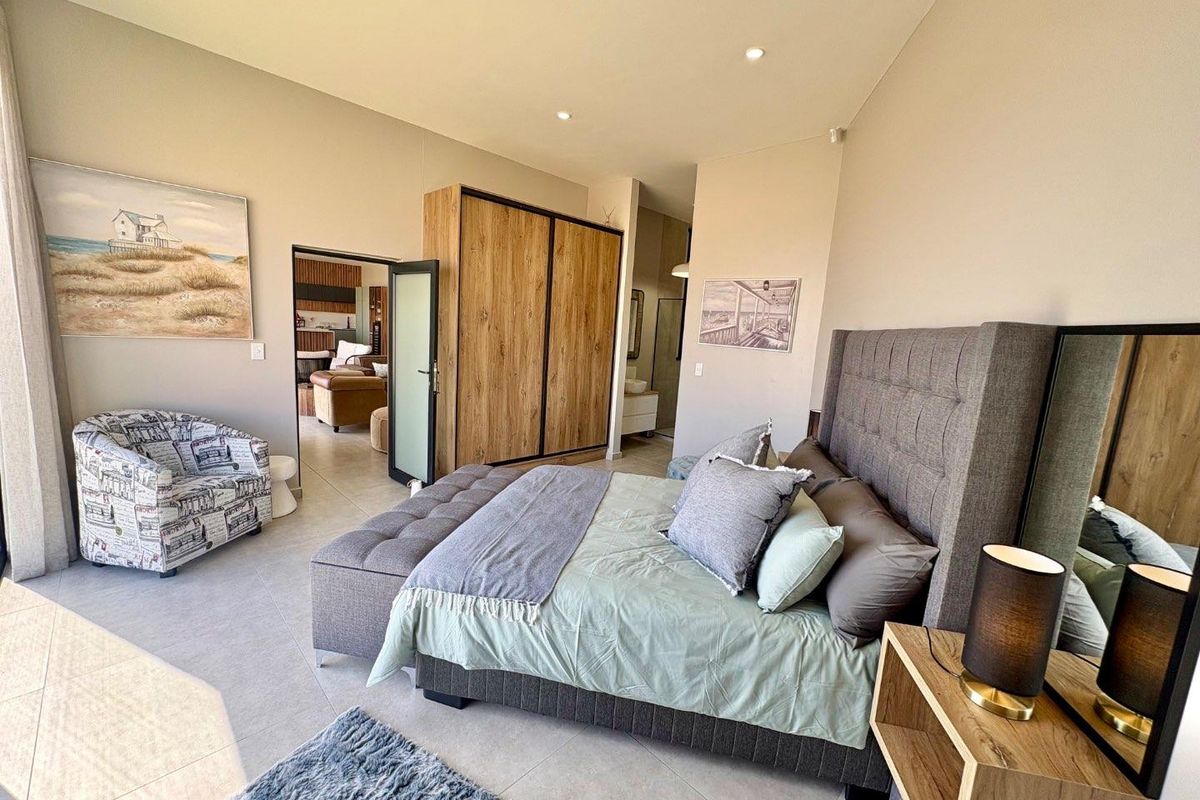 Spacious bedroom featuring built-in wooden cabinetry, recessed ceiling lighting, and tiled flooring, with an adjoining en-suite bathroom visible.