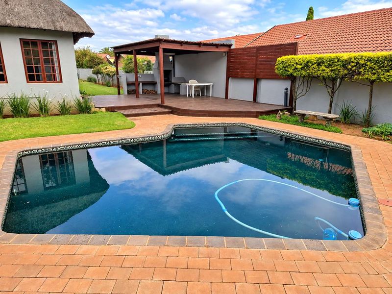 Outdoor entertainment area featuring a swimming pool, paved surround, and a covered timber deck with a built-in braai facility.