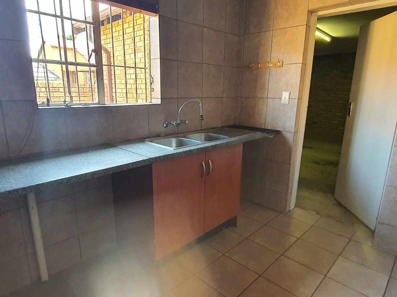 A functional kitchen area featuring tiled walls, a double bowl sink, laminate countertops, and built-in cabinetry, providing a blank canvas for renovation.
