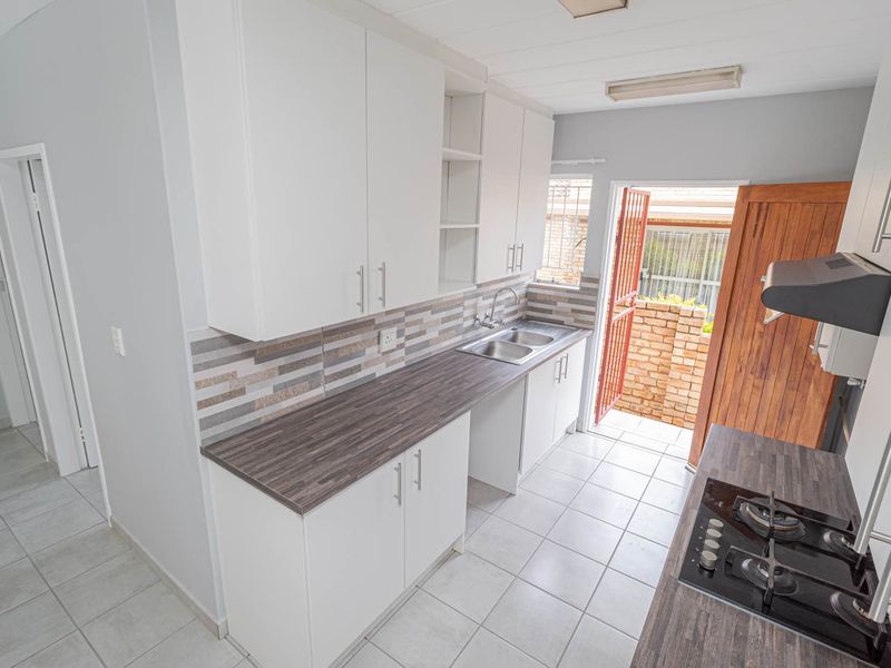 A clean, functional kitchen featuring white cabinetry, dark laminate countertops, a gas hob with extractor, and direct access to an outdoor area.