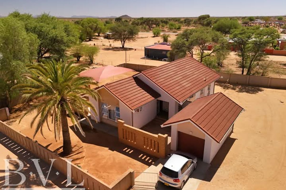 Aerial view of a residential property featuring a tiled roof house, detached garage, brick boundary walls, and a shaded outdoor area.