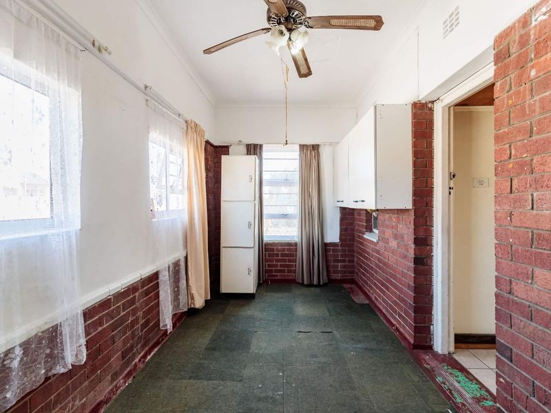 A utility space featuring exposed brick walls, built-in cabinetry, and a ceiling fan, offering a blank canvas for renovation or functional storage.
