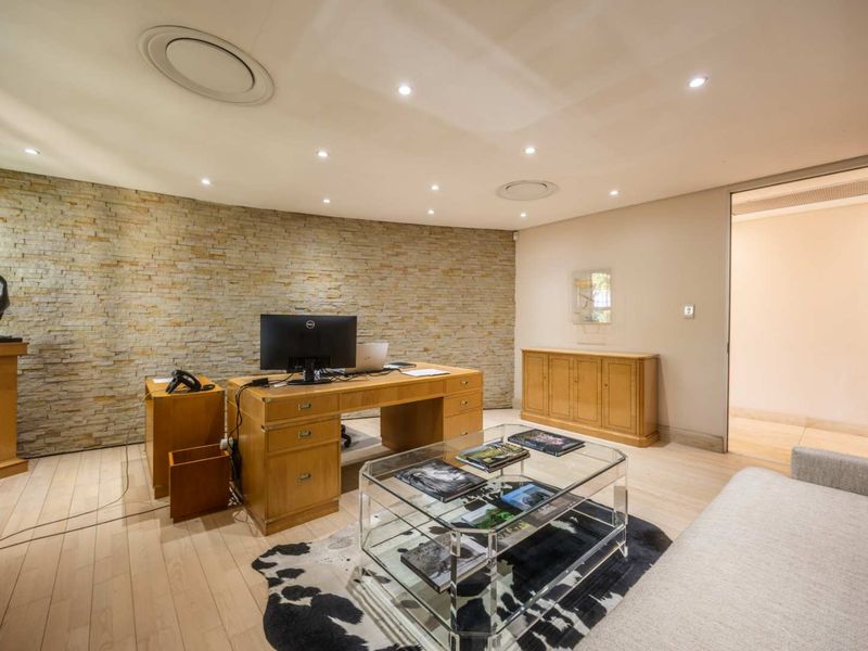 A professional office space featuring a textured stone accent wall, recessed lighting, integrated ceiling speakers, and high-quality hardwood flooring.
