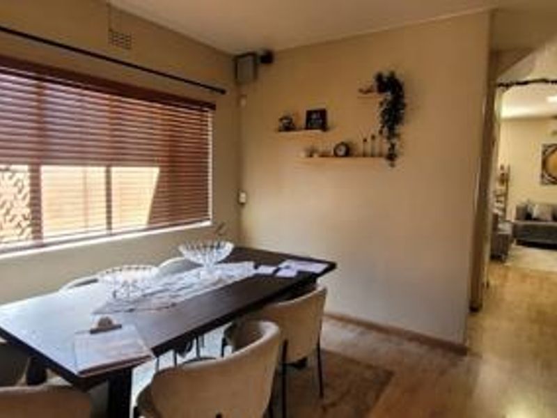 A dining room featuring laminate flooring and venetian blinds, with an open transition to the adjacent living area.