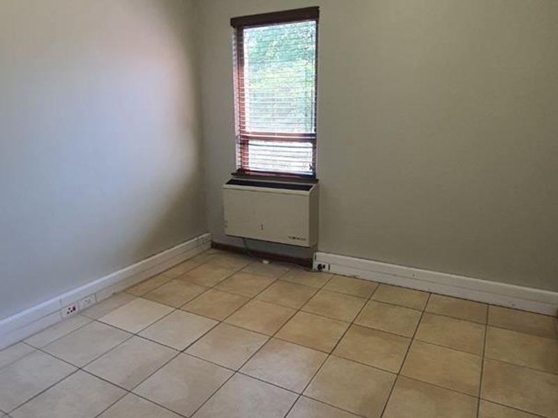 An empty office space featuring tiled flooring, a wall-mounted HVAC unit, and window blinds, suitable for a professional workspace.