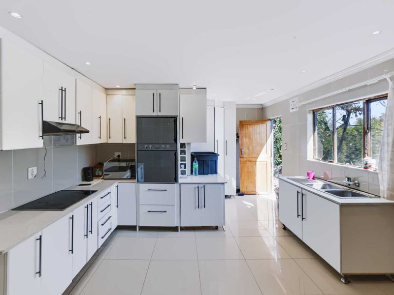 A modern, well-lit kitchen featuring white cabinetry, integrated appliances, a sleek electric hob, and tiled flooring with direct access to the exterior.