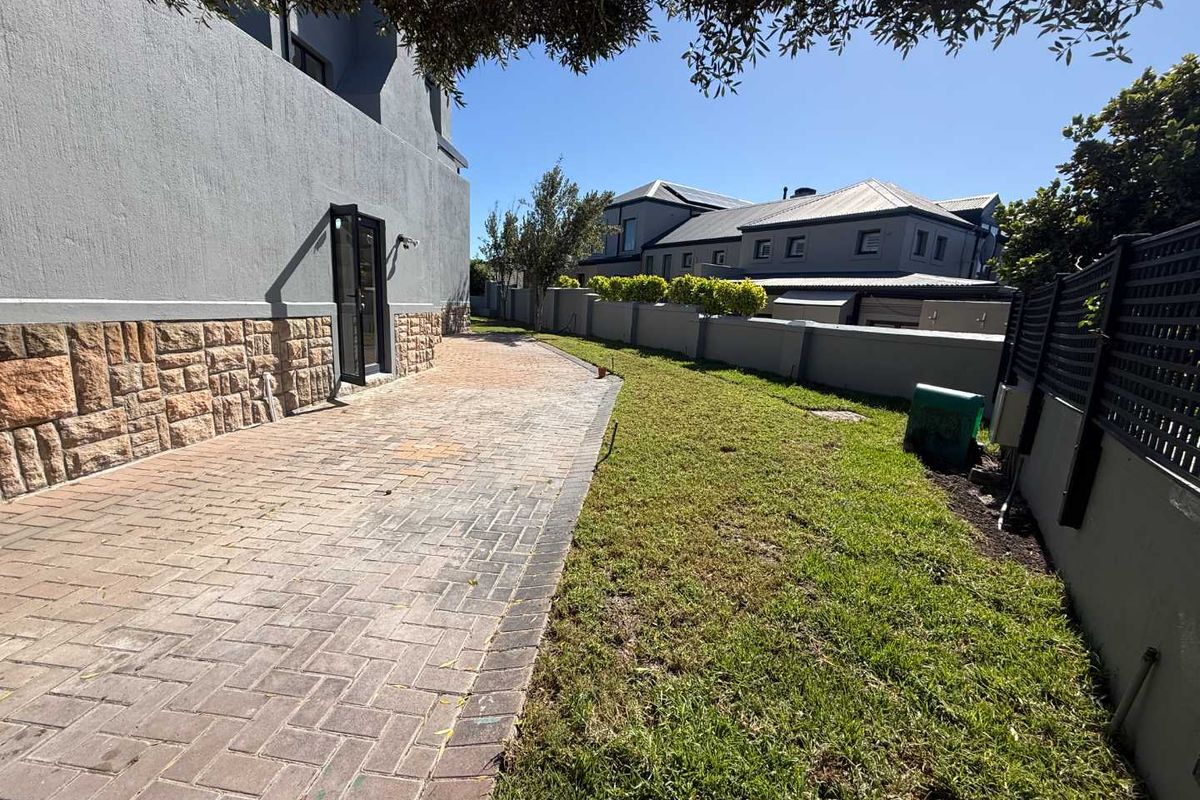 A well-maintained rear exterior area featuring a paved walkway, stone-clad wall detailing, and a neat lawn enclosed by a boundary wall.