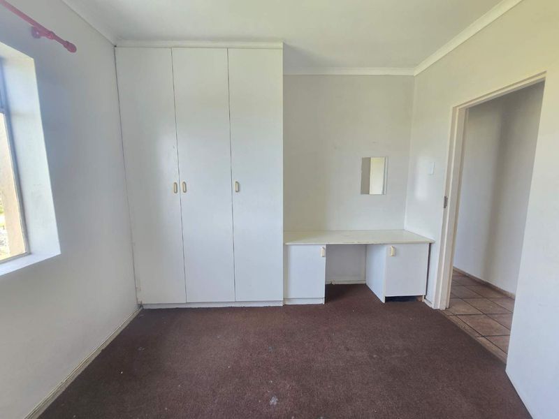 A vacant bedroom featuring built-in wardrobes, a vanity unit, and carpet flooring, offering a blank canvas for potential updates and interior design.