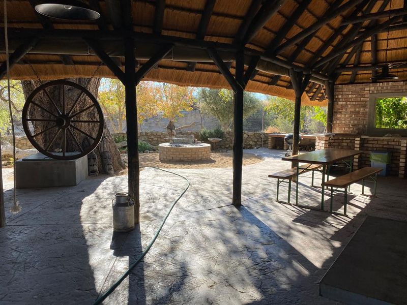 A spacious covered outdoor patio featuring a traditional thatched roof, exposed timber beams, and a built-in brick braai area overlooking the garden.