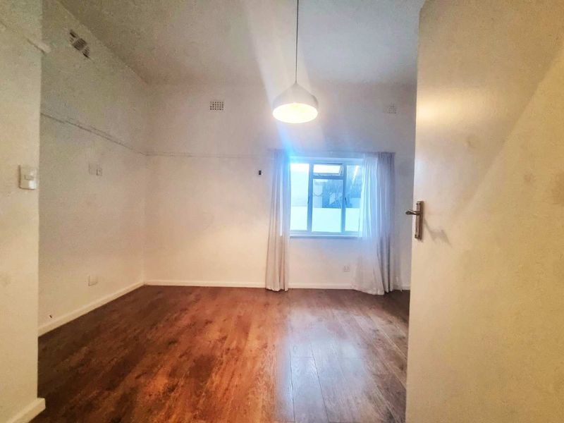 An empty bedroom featuring laminate flooring, a central pendant light, and a window, presenting a blank canvas for potential renovation and styling.