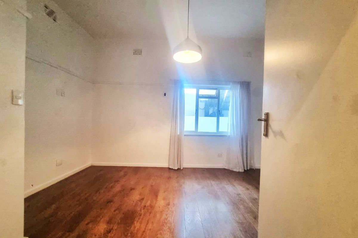 An empty bedroom featuring laminate flooring, a central pendant light, and a window, presenting a blank canvas for potential renovation and styling.