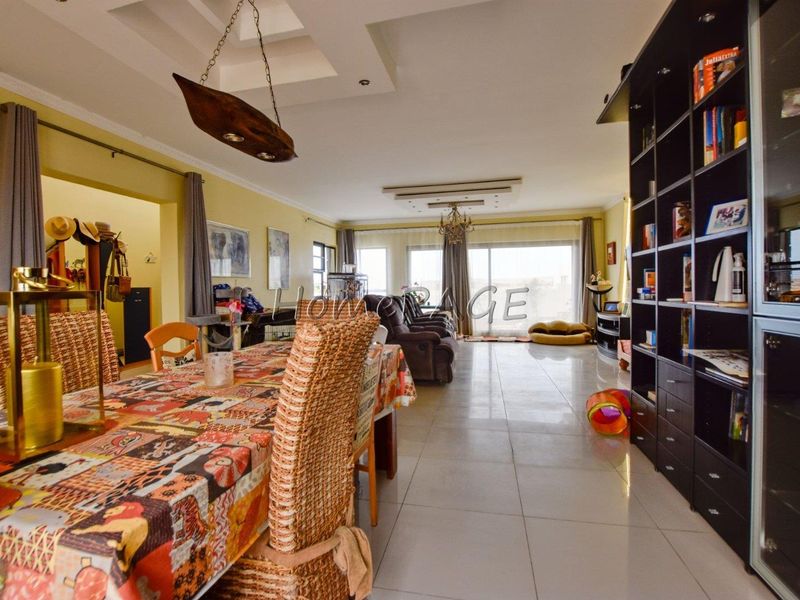 Spacious open-plan living and dining area featuring large format floor tiles, recessed ceiling details, and sliding glass doors leading to the exterior.