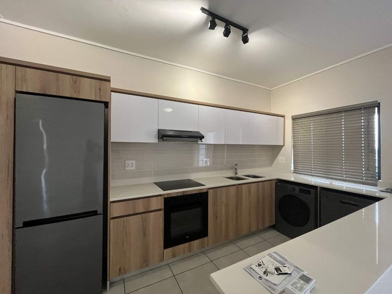 Modern kitchen featuring sleek wood-tone and white cabinetry, quartz countertops, integrated appliances, and contemporary track lighting.