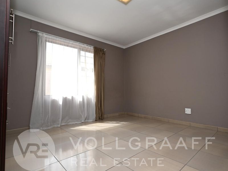 A vacant bedroom featuring neutral wall tones, tiled flooring, and a large window allowing for natural light.