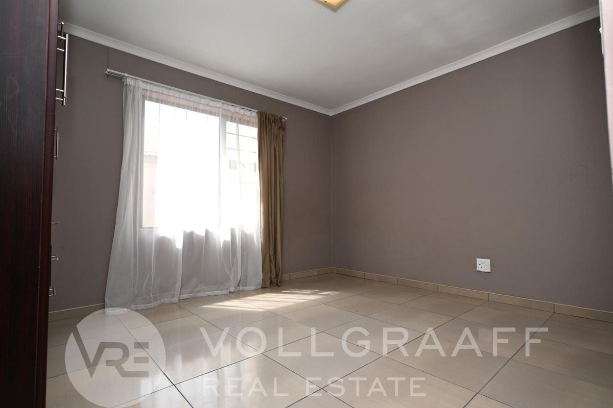 A vacant bedroom featuring neutral wall tones, tiled flooring, and a large window allowing for natural light.
