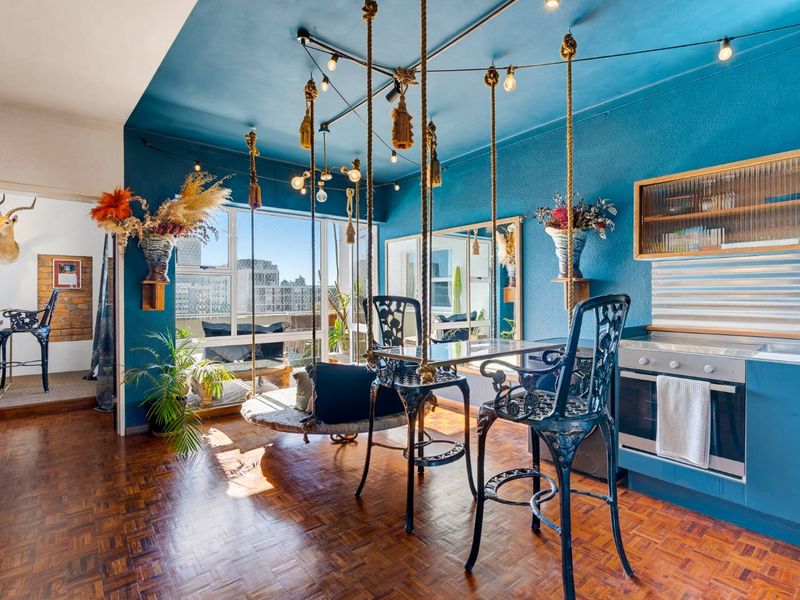 Open-plan living and kitchen area featuring rich parquet flooring, bold blue walls, built-in oven, and large windows providing ample natural light.