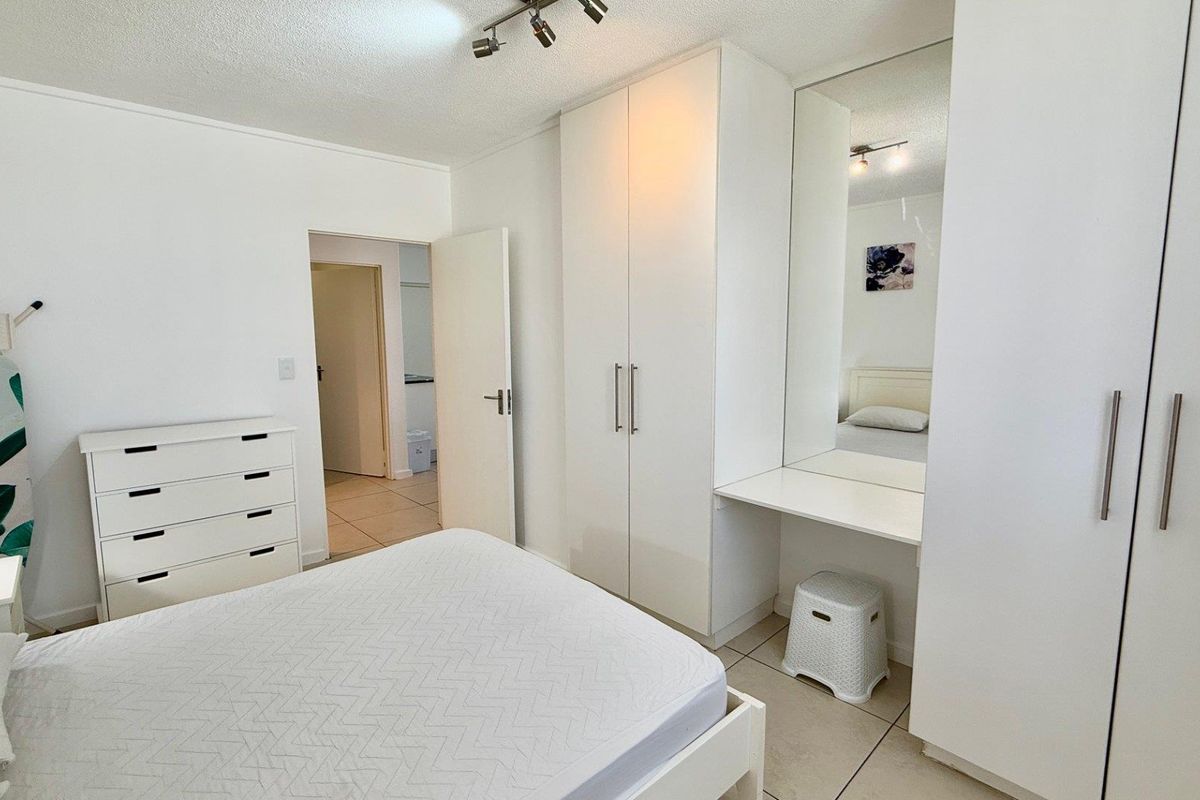 A bright bedroom featuring built-in white cabinetry with an integrated vanity mirror and tiled flooring.