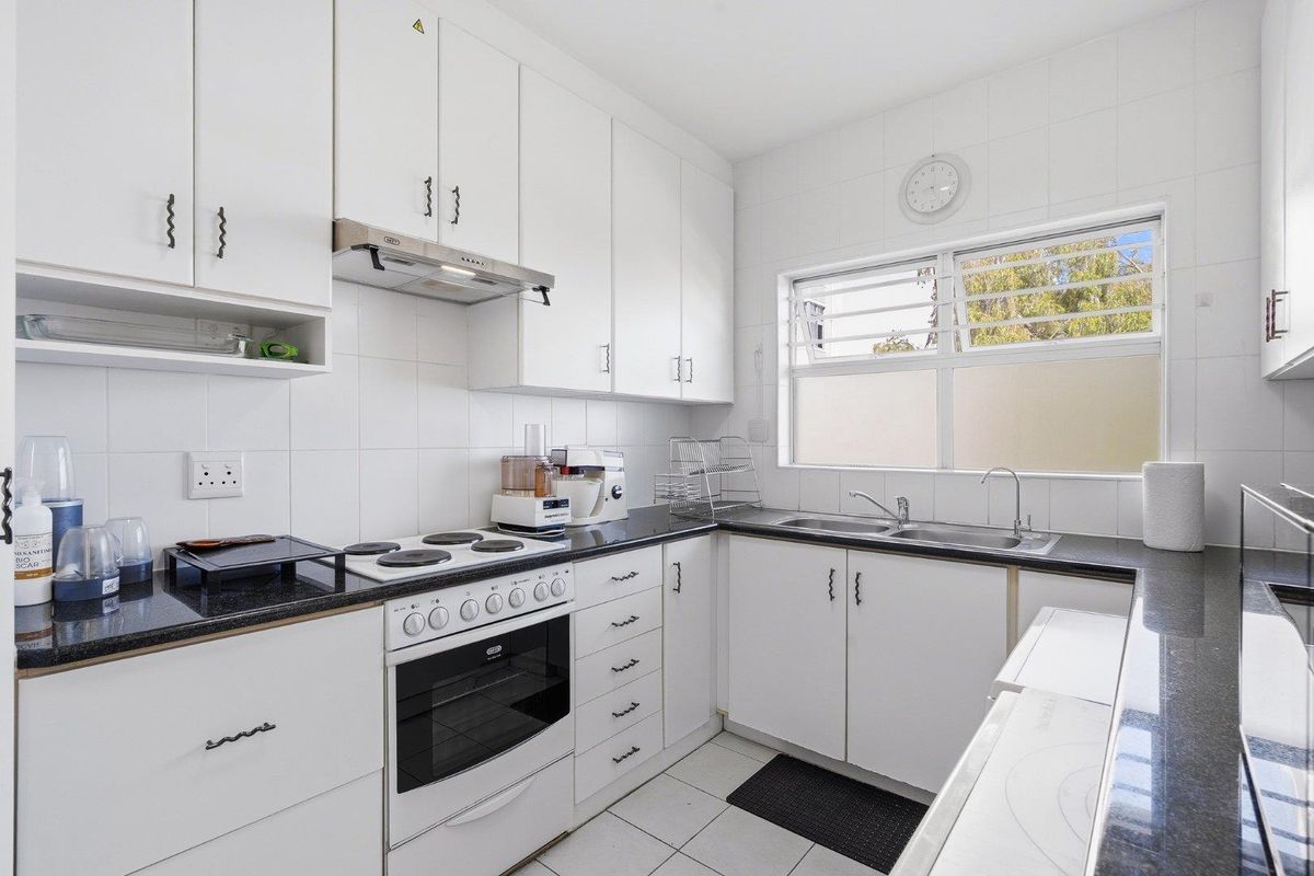 A functional kitchen featuring white cabinetry, black granite countertops, an electric stove with extractor fan, and a double basin sink with tiled finishes.