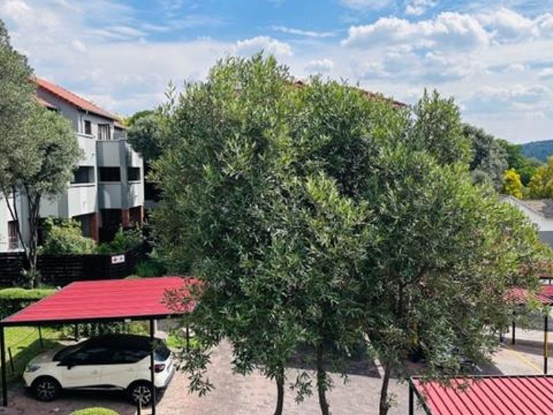 An elevated view of the apartment complex grounds, featuring paved parking areas with covered carports and established garden landscaping.