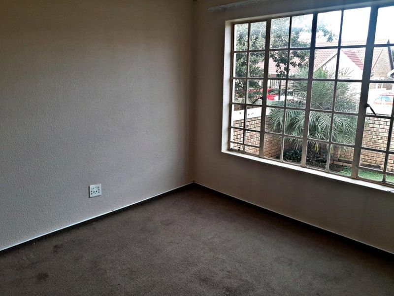 An empty bedroom featuring a large grid-pattern window, neutral wall finishes, and carpeted flooring, offering a blank canvas for potential interior design updates.