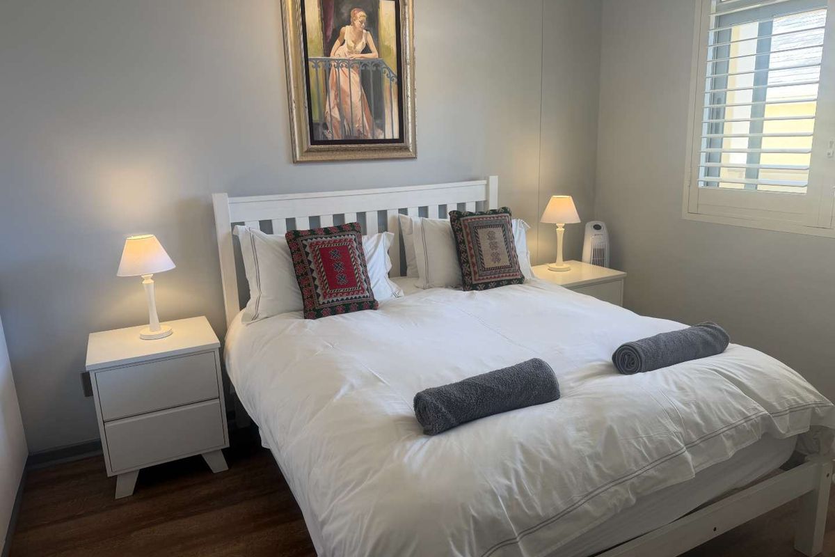 A well-maintained bedroom featuring wood-look flooring and plantation shutters, providing a clean and comfortable living space.