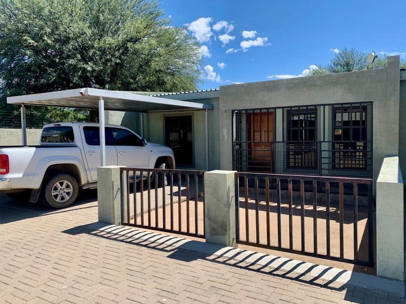Front exterior view of the apartment featuring a paved driveway, covered carport, and secure metal fencing and window bars.