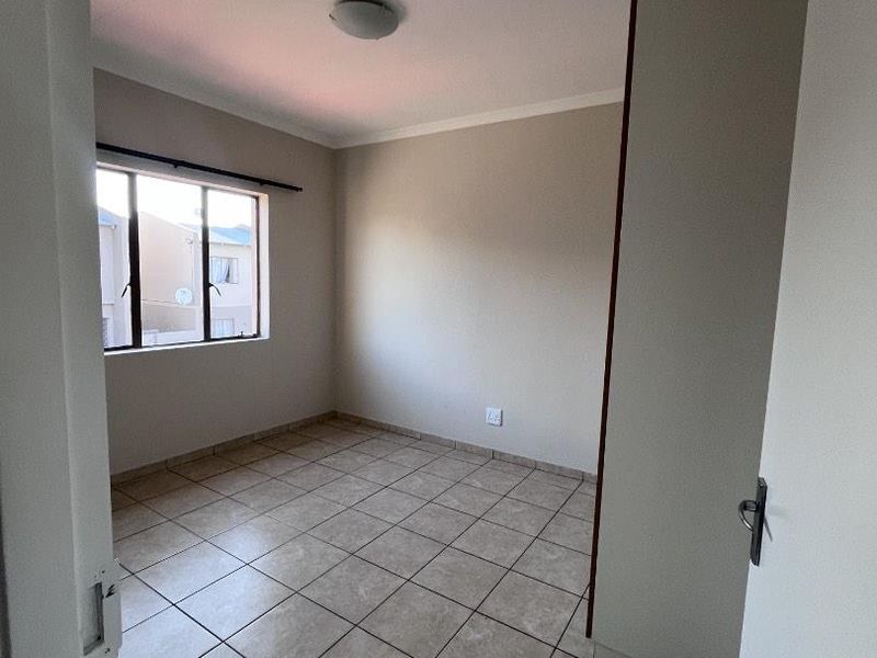An empty bedroom featuring neutral tiled flooring, a built-in cupboard, and a window providing natural light.