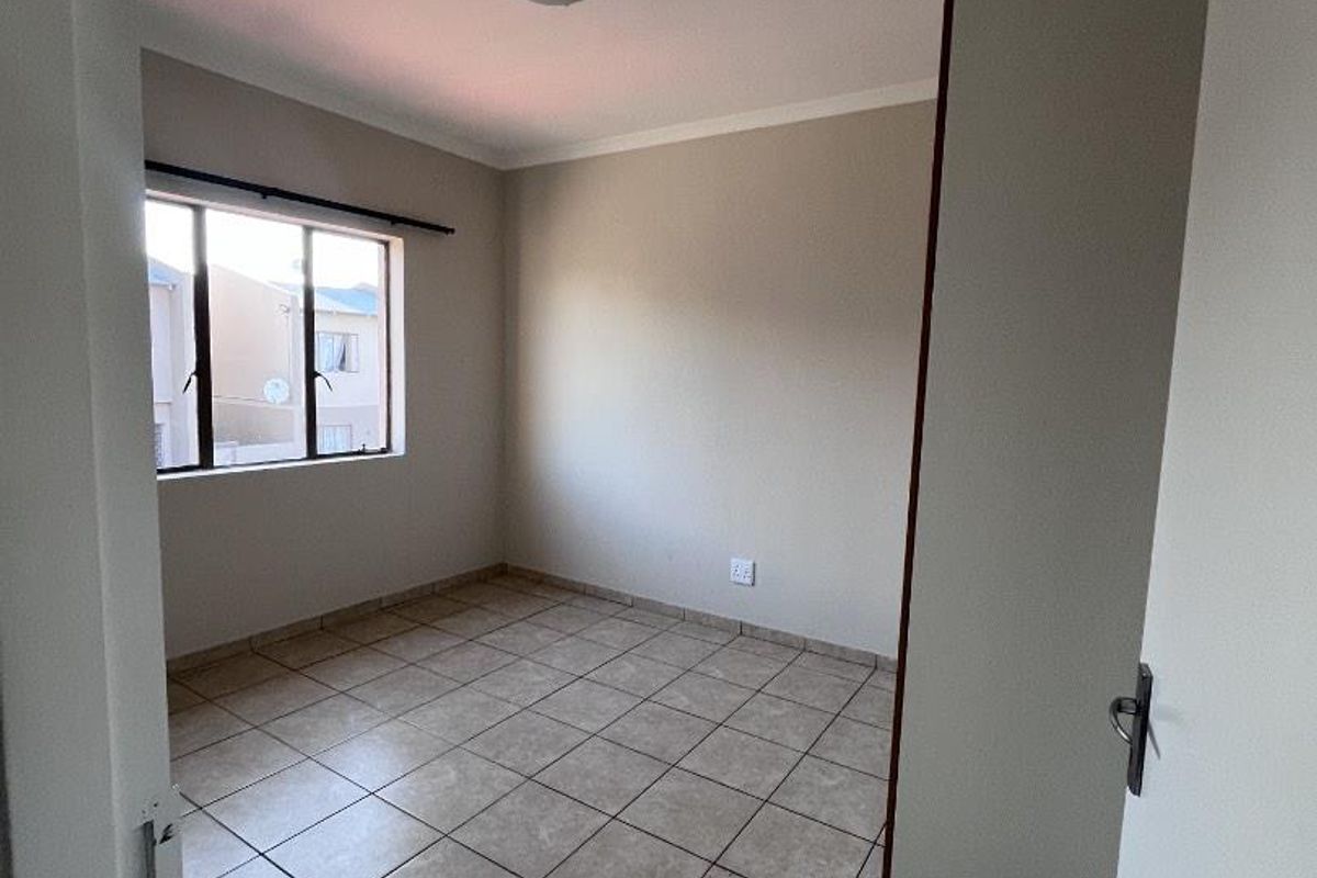 An empty bedroom featuring neutral tiled flooring, a built-in cupboard, and a window providing natural light.