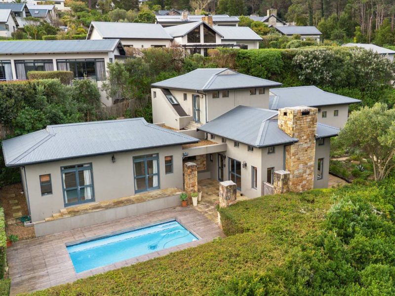 Aerial view of a modern residential property featuring a swimming pool, timber decking, stone chimney, and well-maintained landscaped gardens in a scenic estate setting.