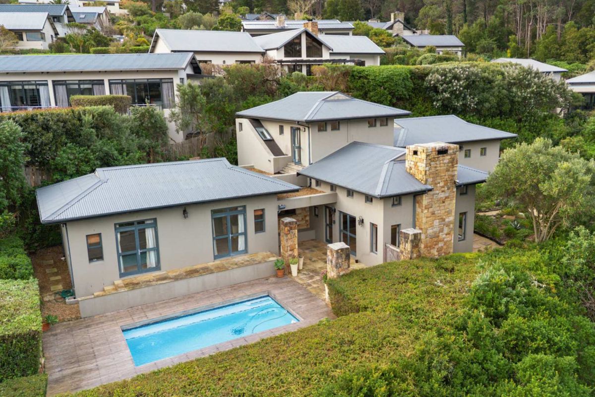 Aerial view of a modern residential property featuring a swimming pool, timber decking, stone chimney, and well-maintained landscaped gardens in a scenic estate setting.