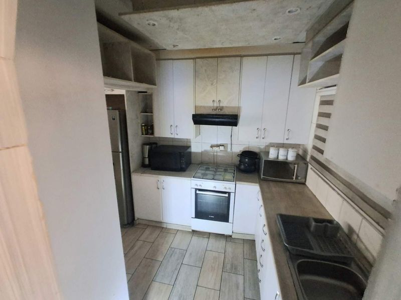 Compact kitchen featuring white cabinetry, gas hob, electric oven, and tiled flooring. The space requires ceiling finishing and minor cosmetic updates.