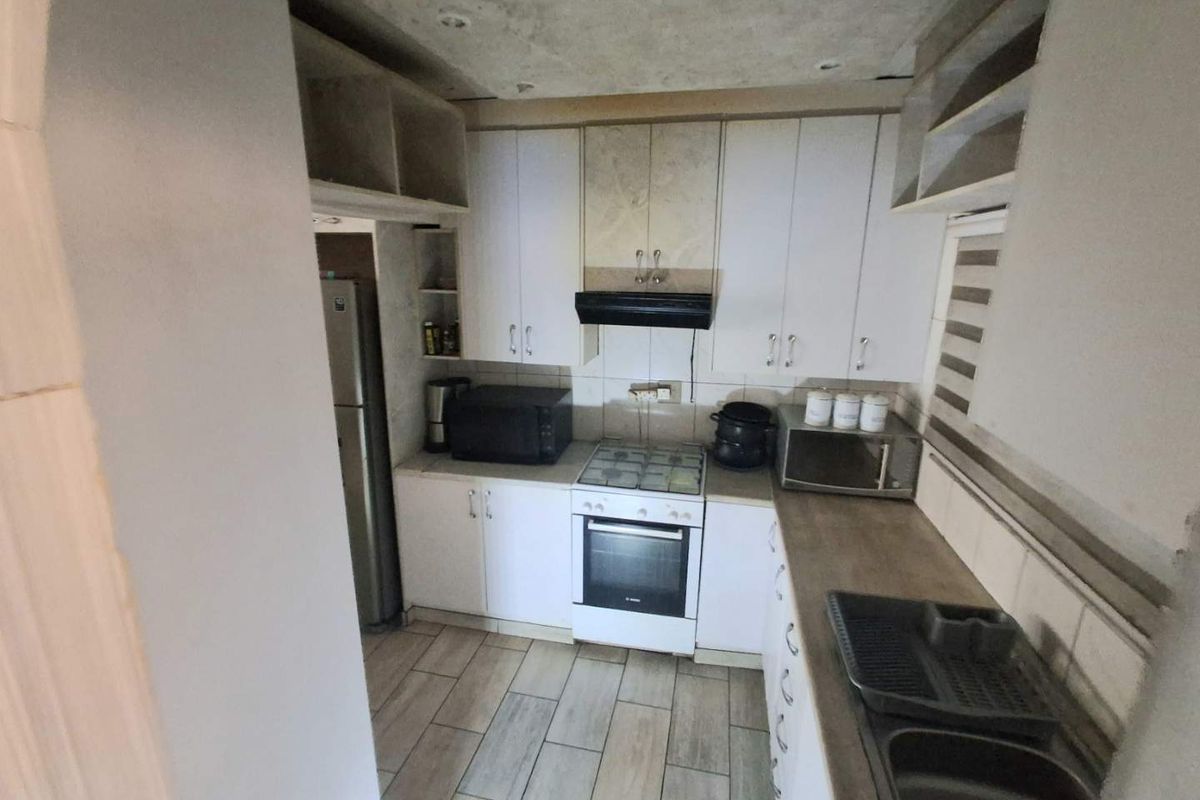 Compact kitchen featuring white cabinetry, gas hob, electric oven, and tiled flooring. The space requires ceiling finishing and minor cosmetic updates.