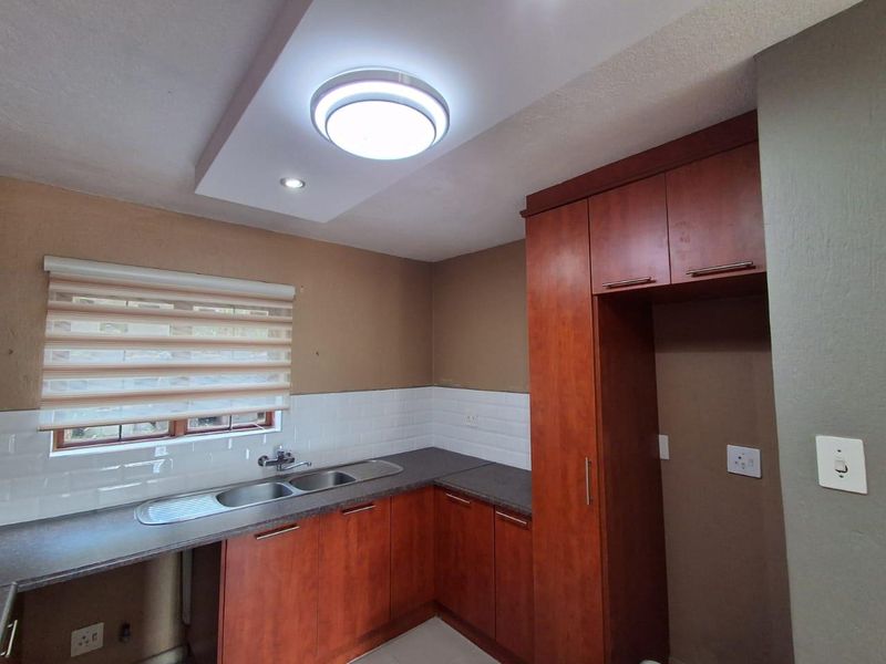 A functional kitchen featuring wood-finish cabinetry, dark countertops, a stainless steel double sink, and a clean white subway tile backsplash.