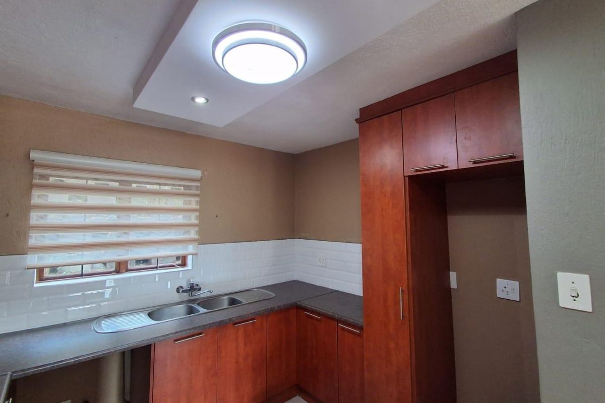 A functional kitchen featuring wood-finish cabinetry, dark countertops, a stainless steel double sink, and a clean white subway tile backsplash.