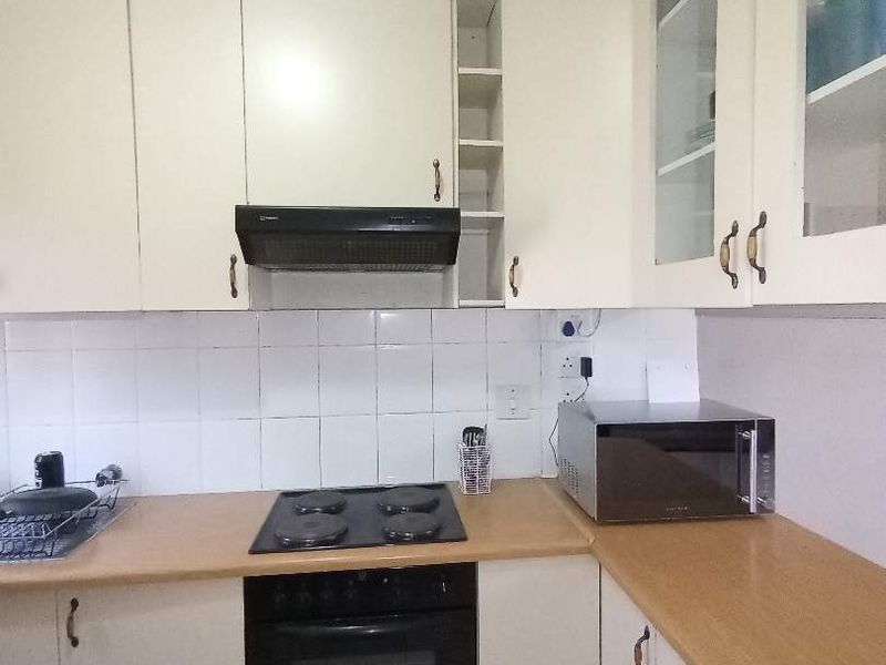 A functional kitchen featuring built-in cabinetry, a laminate countertop, an electric hob, an oven, and a tiled backsplash.