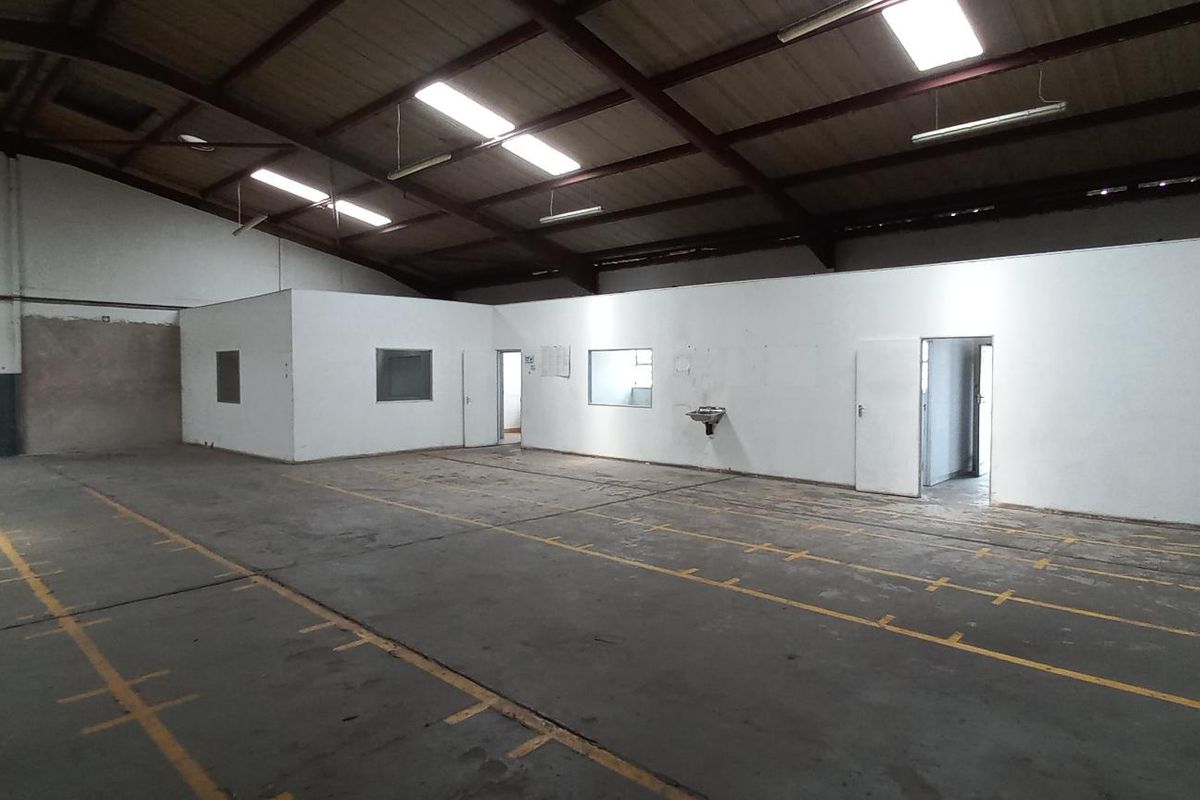 Spacious industrial warehouse featuring high ceilings, exposed steel trusses, concrete flooring with marked bays, and partitioned office or utility rooms.