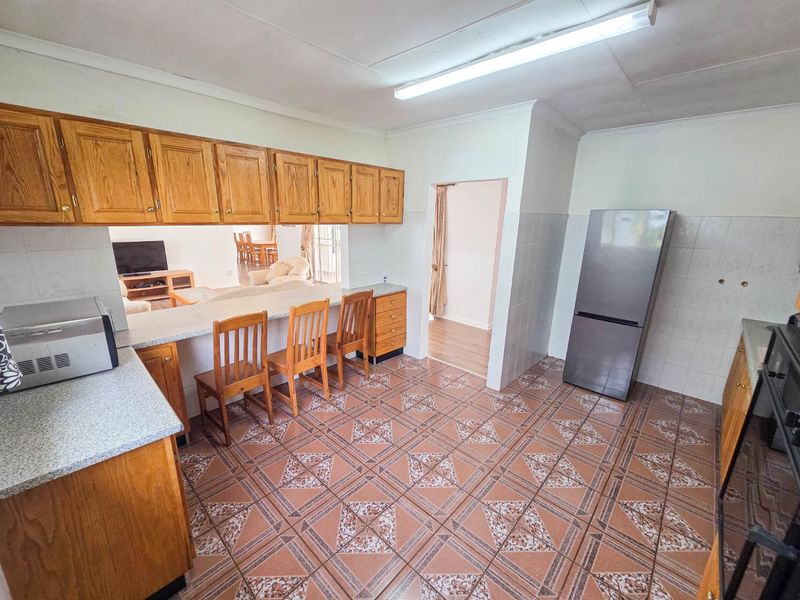 A functional kitchen featuring wooden cabinetry, a breakfast bar, and tiled flooring, offering an open-plan layout connected to the living area.