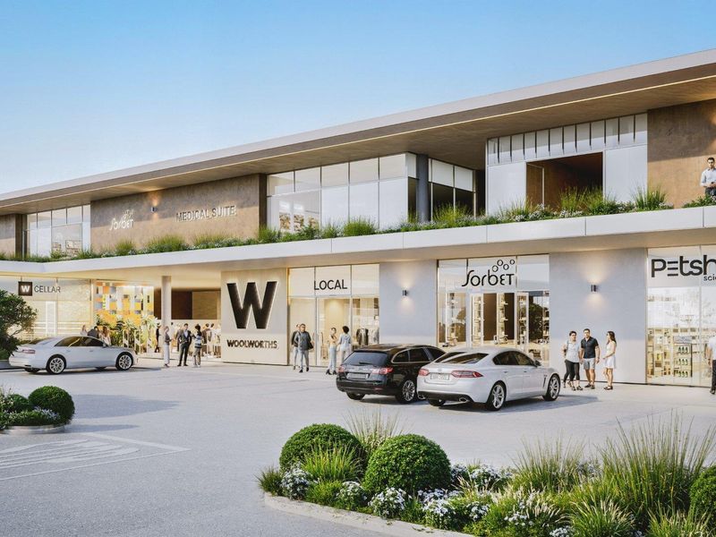 Modern commercial retail center featuring multiple storefronts, large glass display windows, and a paved parking area with landscaped garden beds.